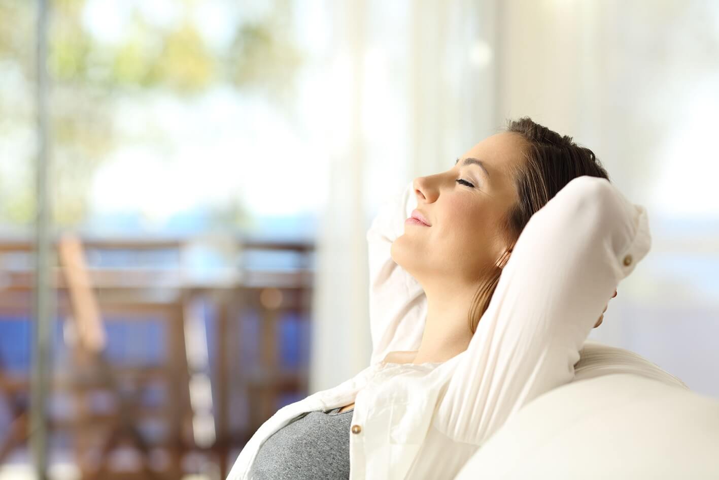 Frau atmet entspannt zurückgelehnt auf dem Sofa tief ein (Raumluftfilter)
