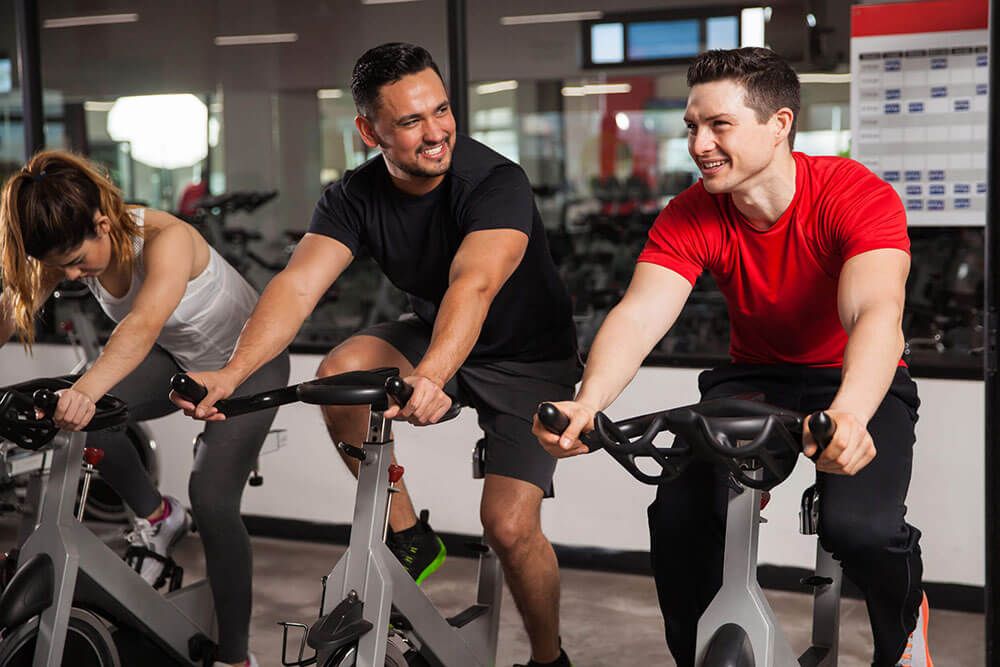 Portrait of a couple of young men talking and laughing while doing some spinning at a gym
